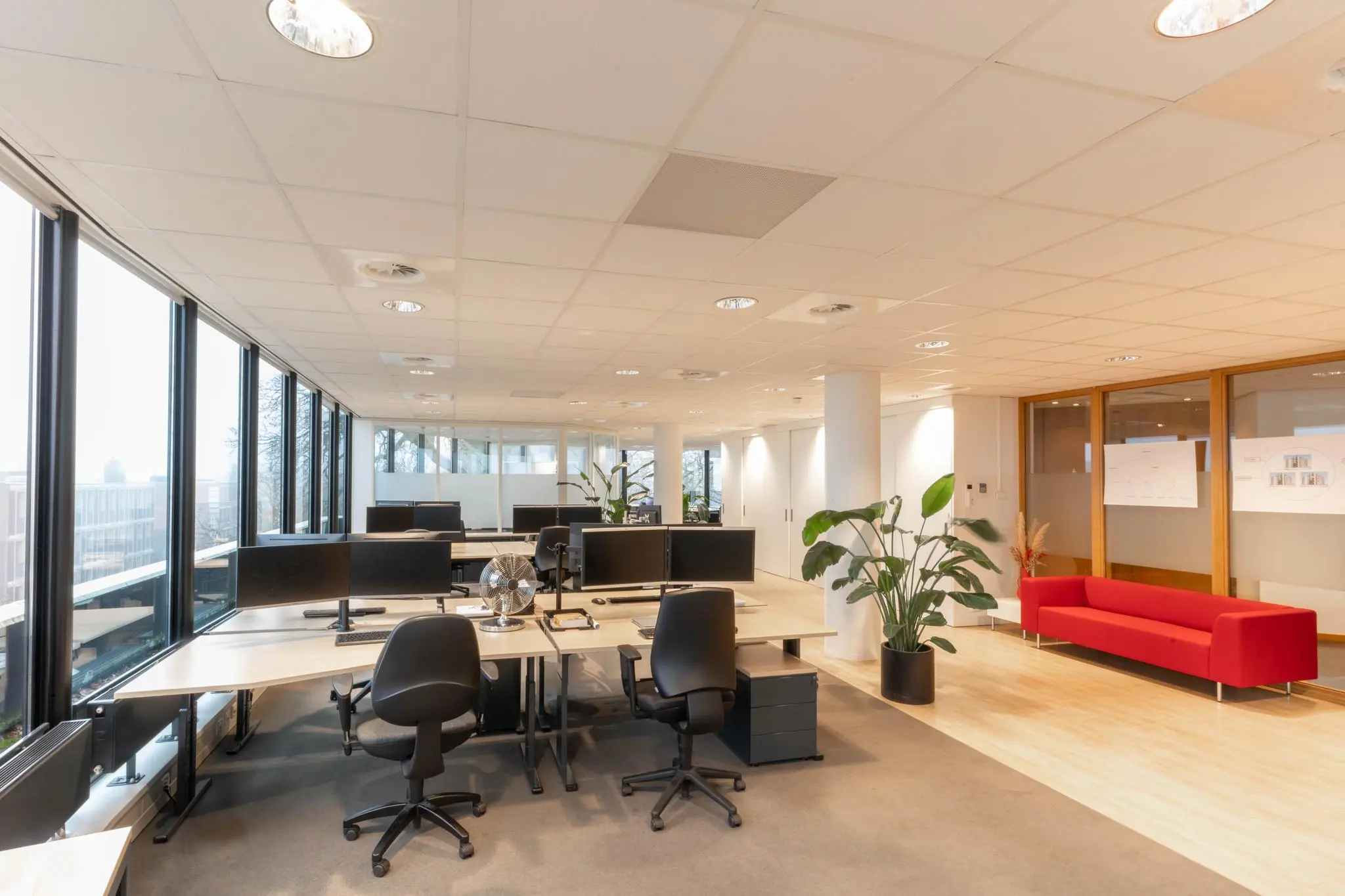 Modern en licht kantoorinterieur aan de 1e Hogeweg met bureaus, computers, planten en een rode bank in de wachtruimte.